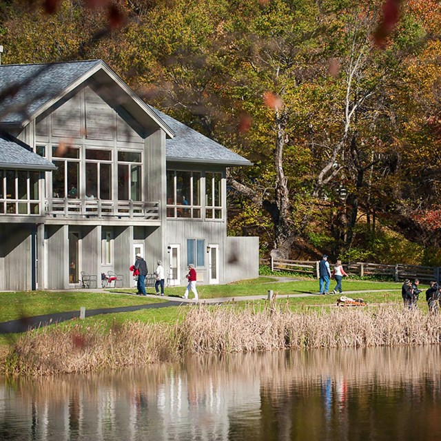 A lodge at the edge of a lake, with a autumn forest in the background