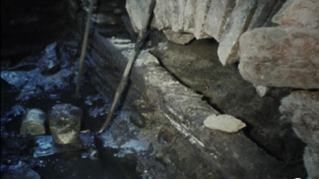 Color photograph of an archeological dig with stone walls and muddy floor