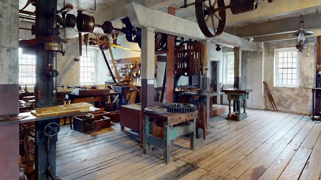  Interior of Wilkinson Mill: Wooden floors, beams, large machinery, benches, tools, and sunlit windo