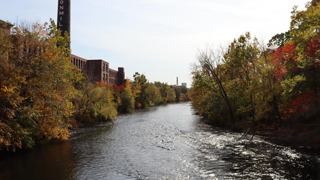 Photo of the Blackstone River with Ashton Mill on the left side and surrounded by trees