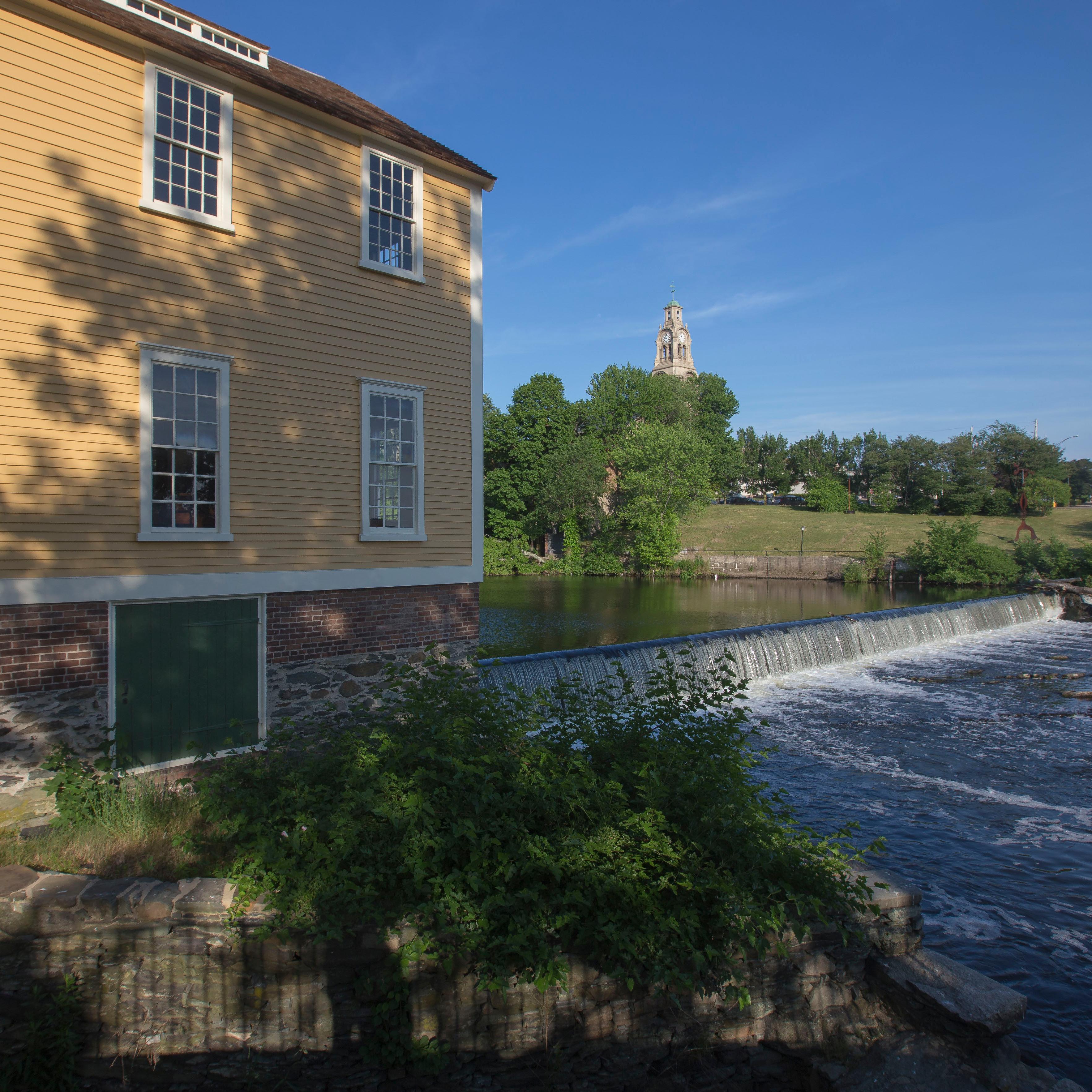 Slater Mill Dam across the Blackstone River causing waterfall and yellow wooden building on left