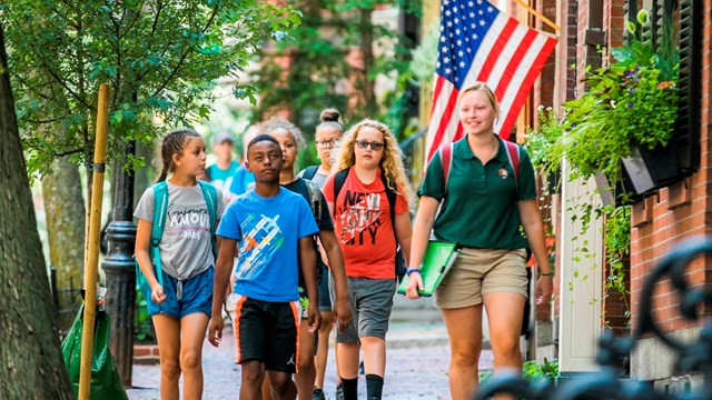 a young woman with a NPS polo walks down the street with some kids.