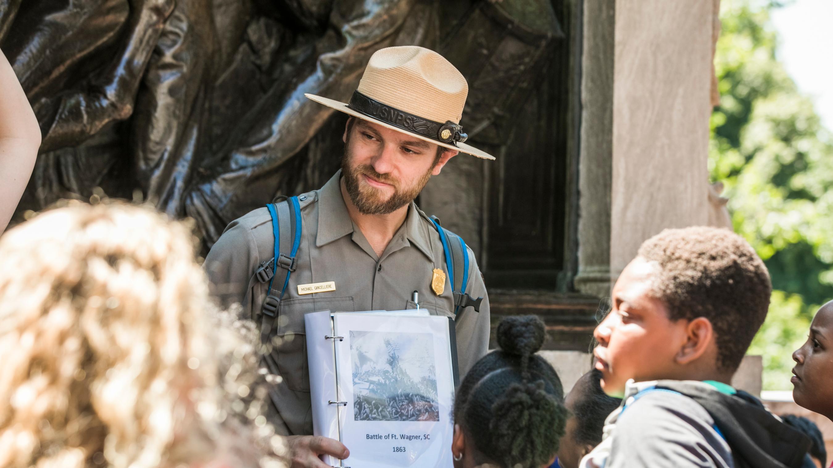 A male park ranger holds an image out for a group of students to look at.