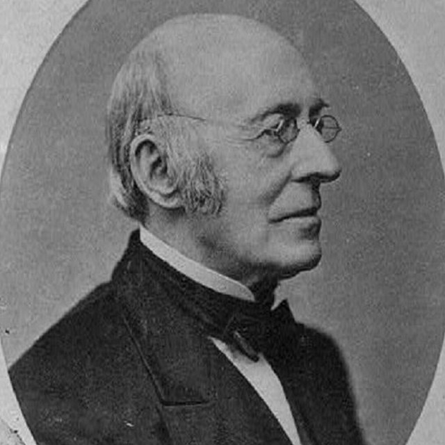 Profile photograph of William Lloyd Garrison, a White man with short light hair and glasses. 