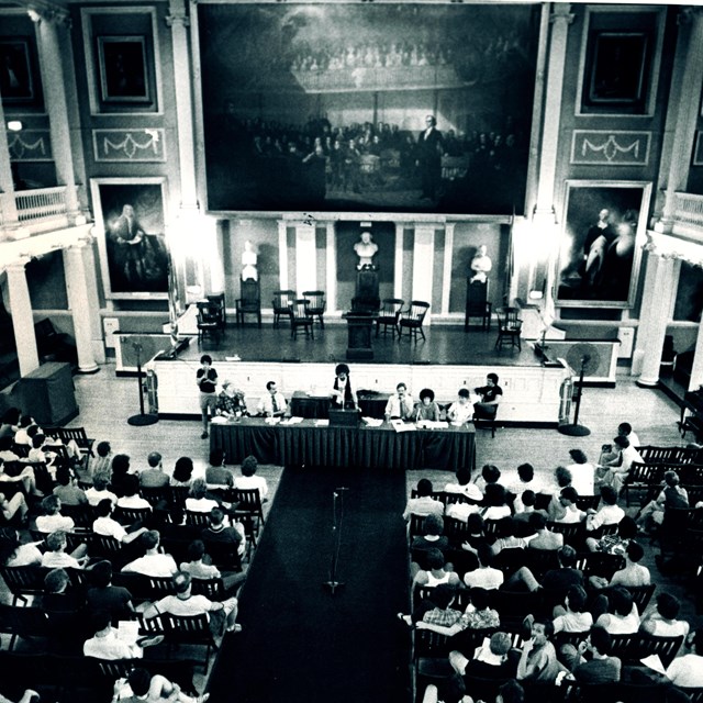 Aerial view of the Great Hall in Faneuil Hall with people sitting in chairs. 