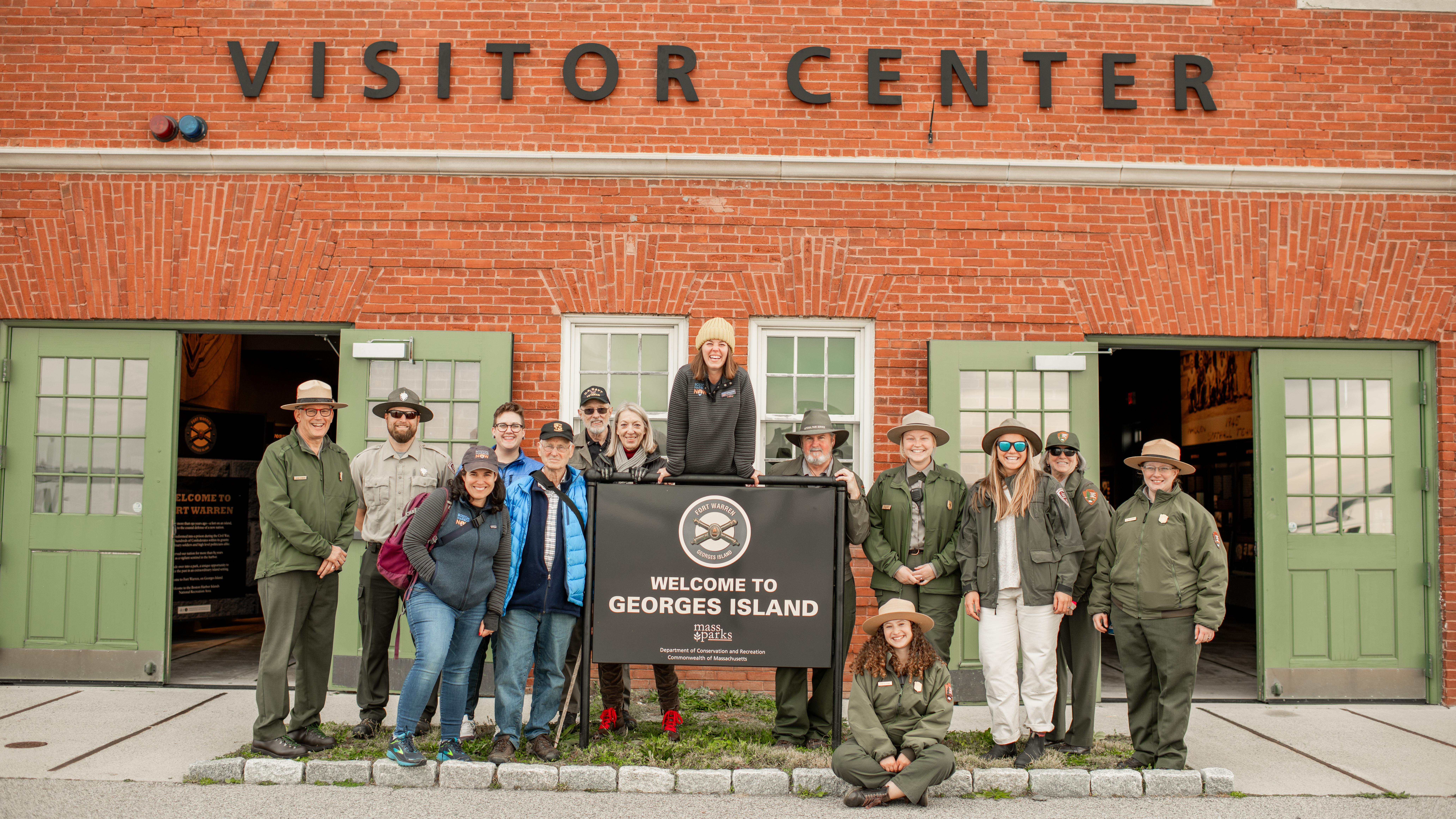 Group of DCR and NPS rangers with other partners around Georges Island sign.