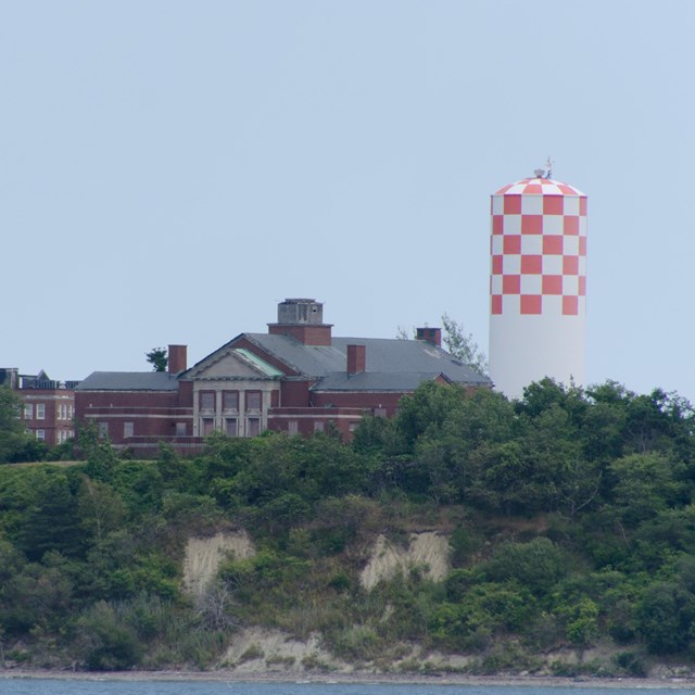 A white and red-checkered watertower and a brick building sit atop a bluff of an island.