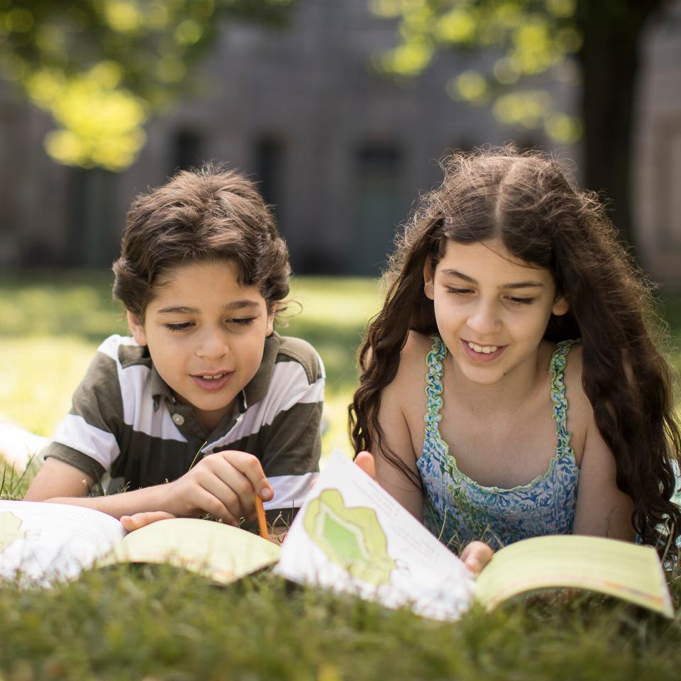 Two children laying in the grass work on Junior Ranger books.