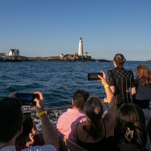 People on a boat taking pictures or looking at a white lighthouse on a rocky island 
