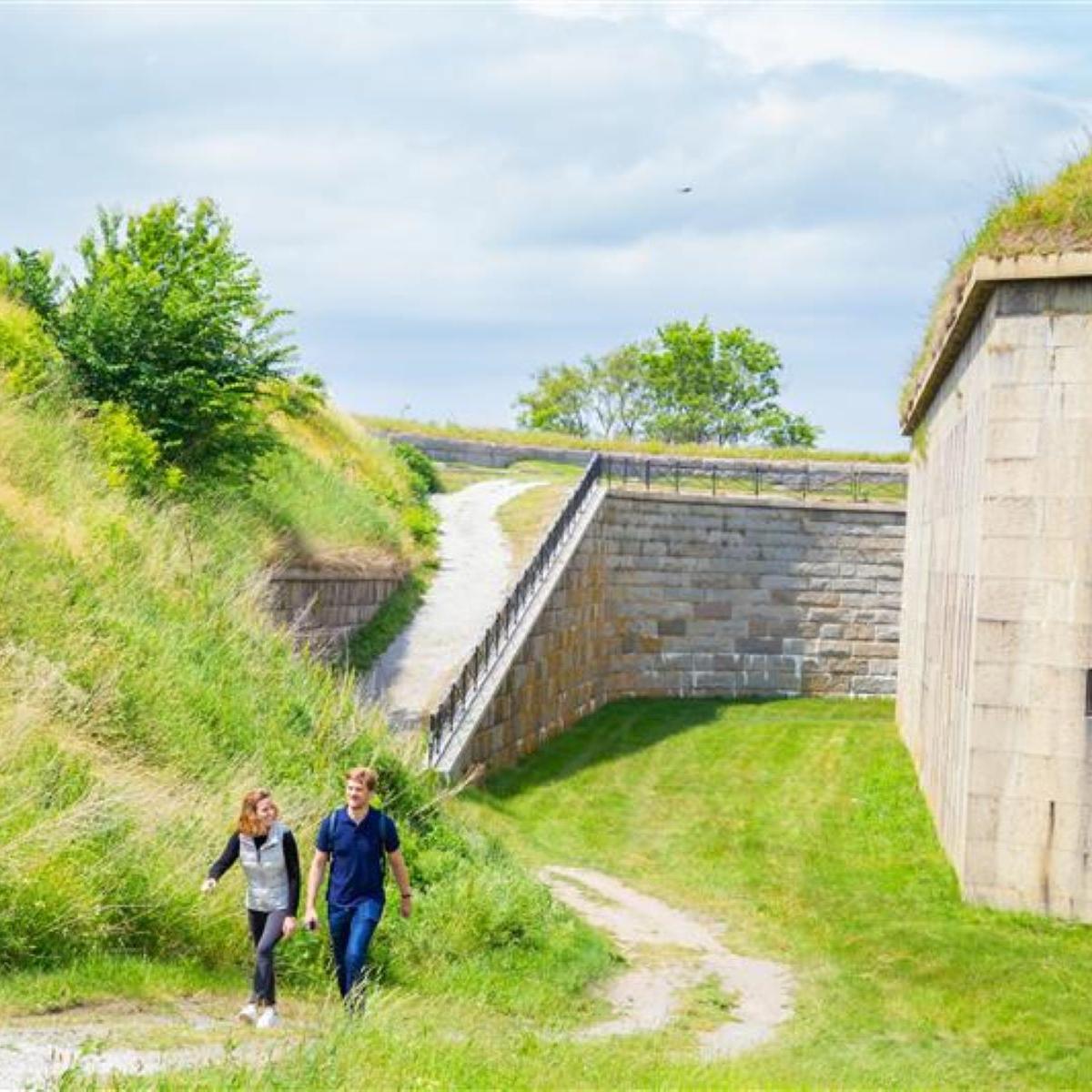Two people walking on a trail with a forts granite wall to the left of them