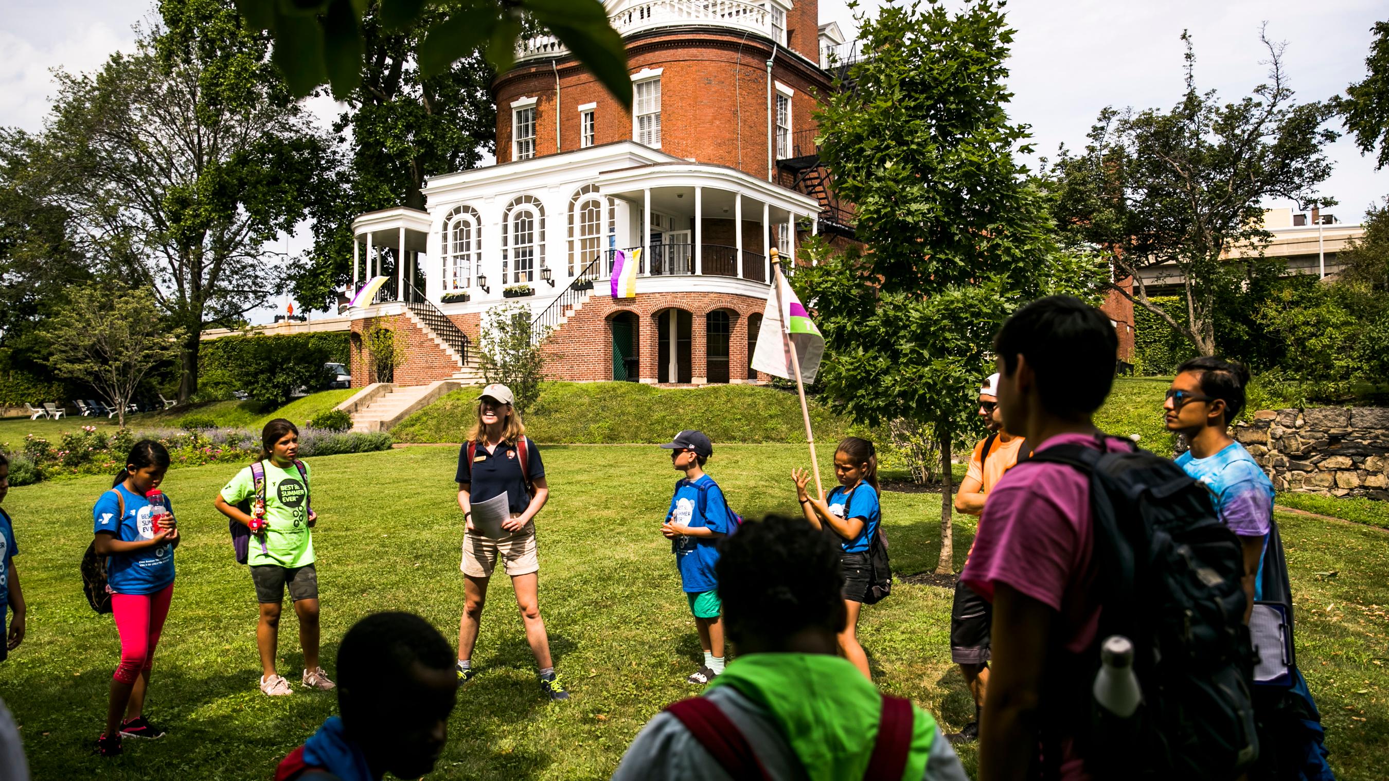 circle of kids and education team member on grassy lawn in front of commandant's house.