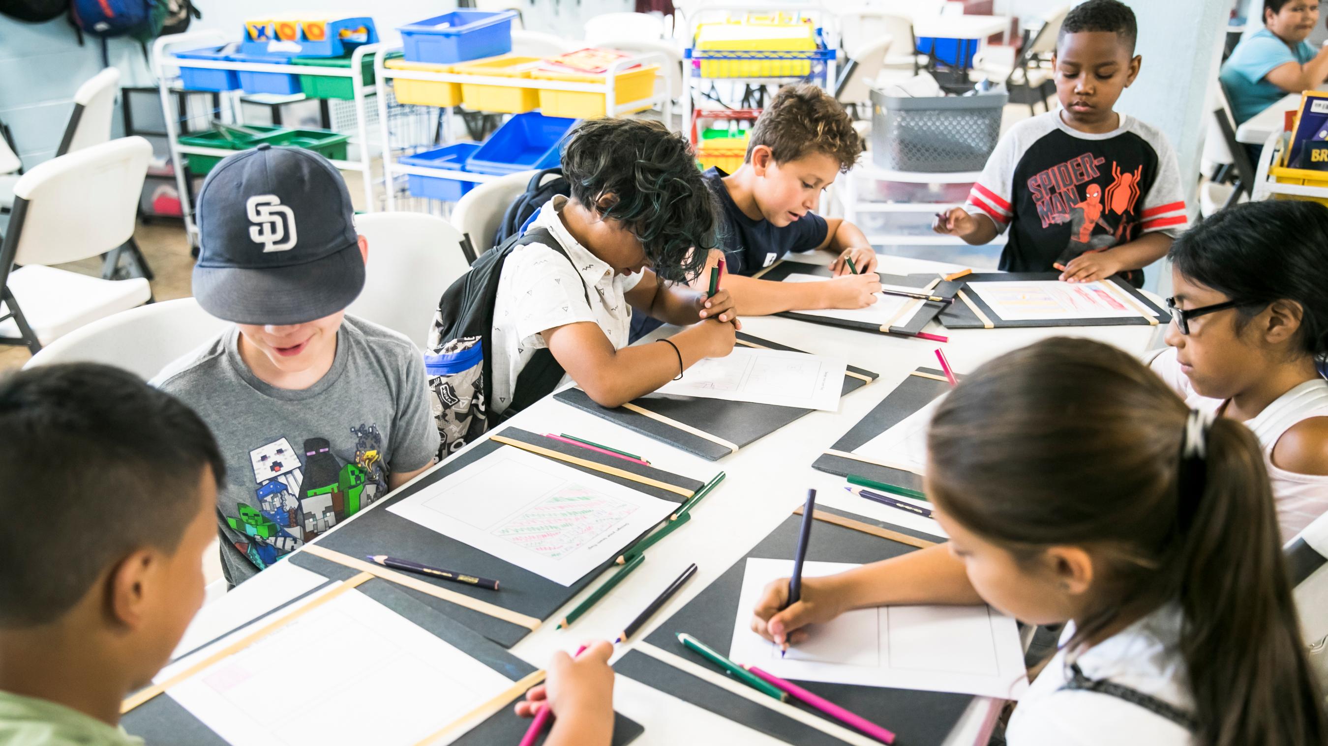 group of students sitting around a table drawing and writing.