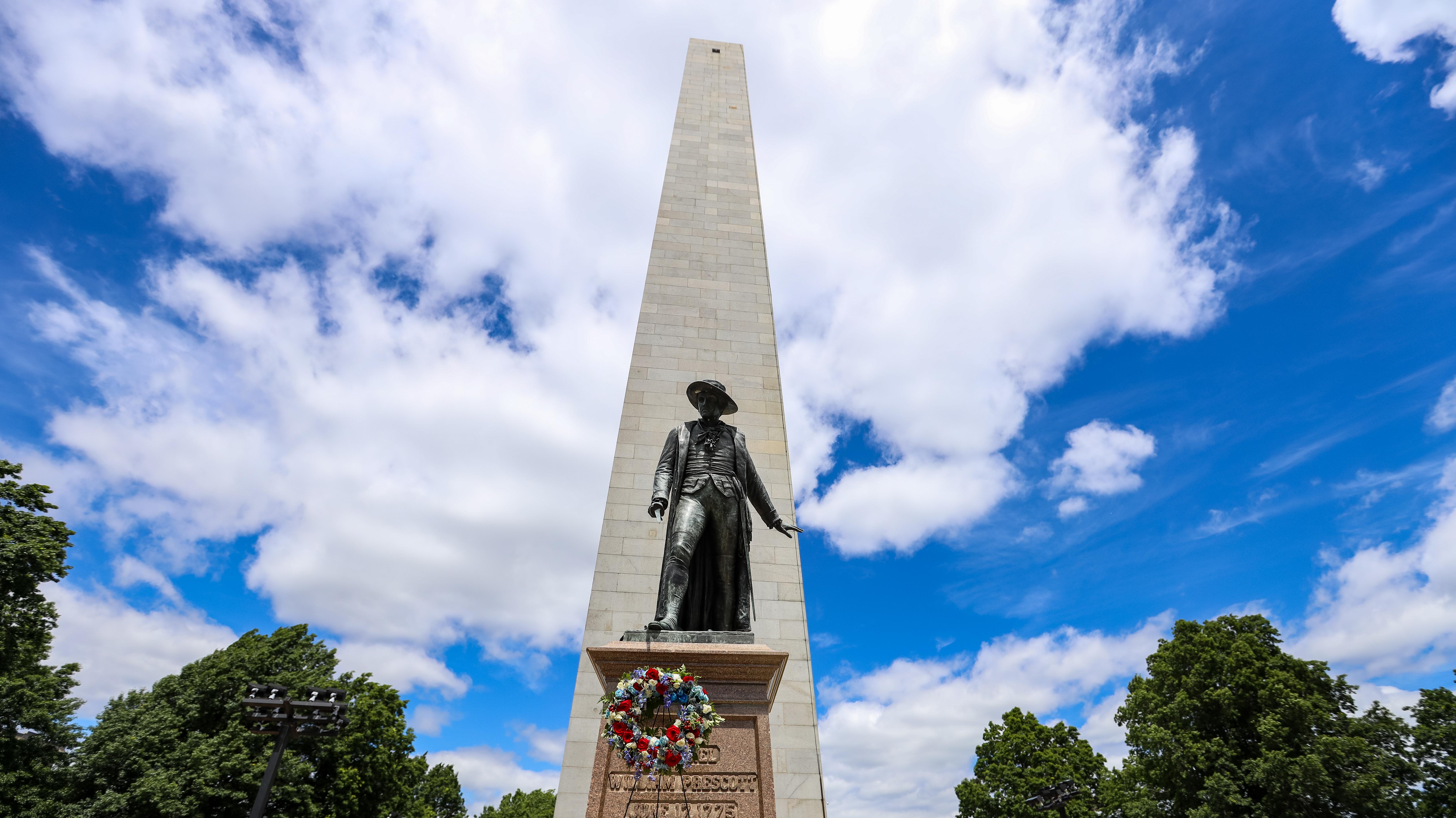 Bunker Hill Monument and William Prescott statue with a floral wreath on a partly cloudy day.