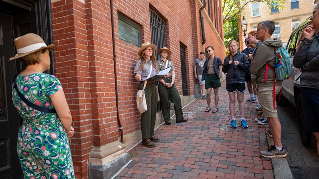 Two Park Rangers stand in front of a crowd next to a brick building