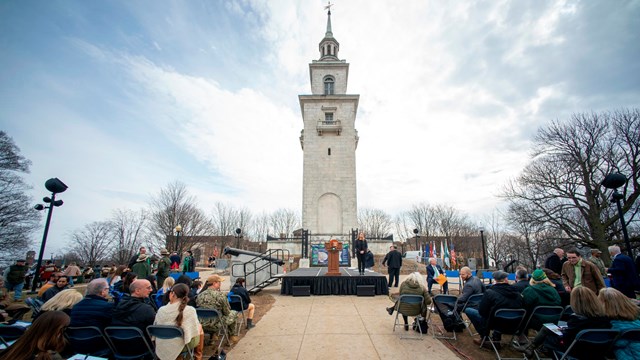 Dorchester Heights Monument with stage and podium in front and audience on either side of sidewalk.