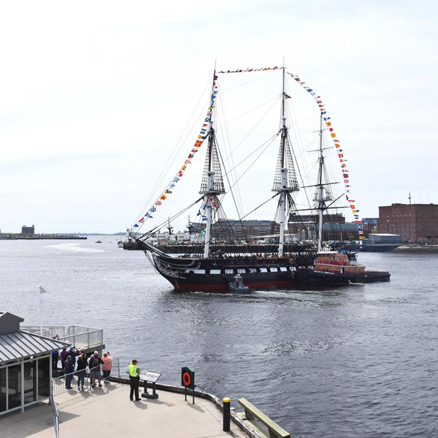 USS CONSTITUTION adorned in signal flags sails through Boston Harbor.