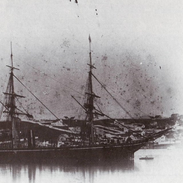 Three-masted ship docked in a harbor. 