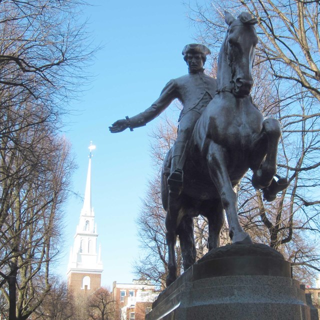 A bronze statue of Paul Revere riding a horse with the white steeple of Old North in background