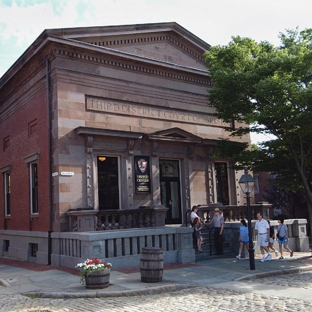 Side and partial front view of the park visitor center, a brick building with a pediment.