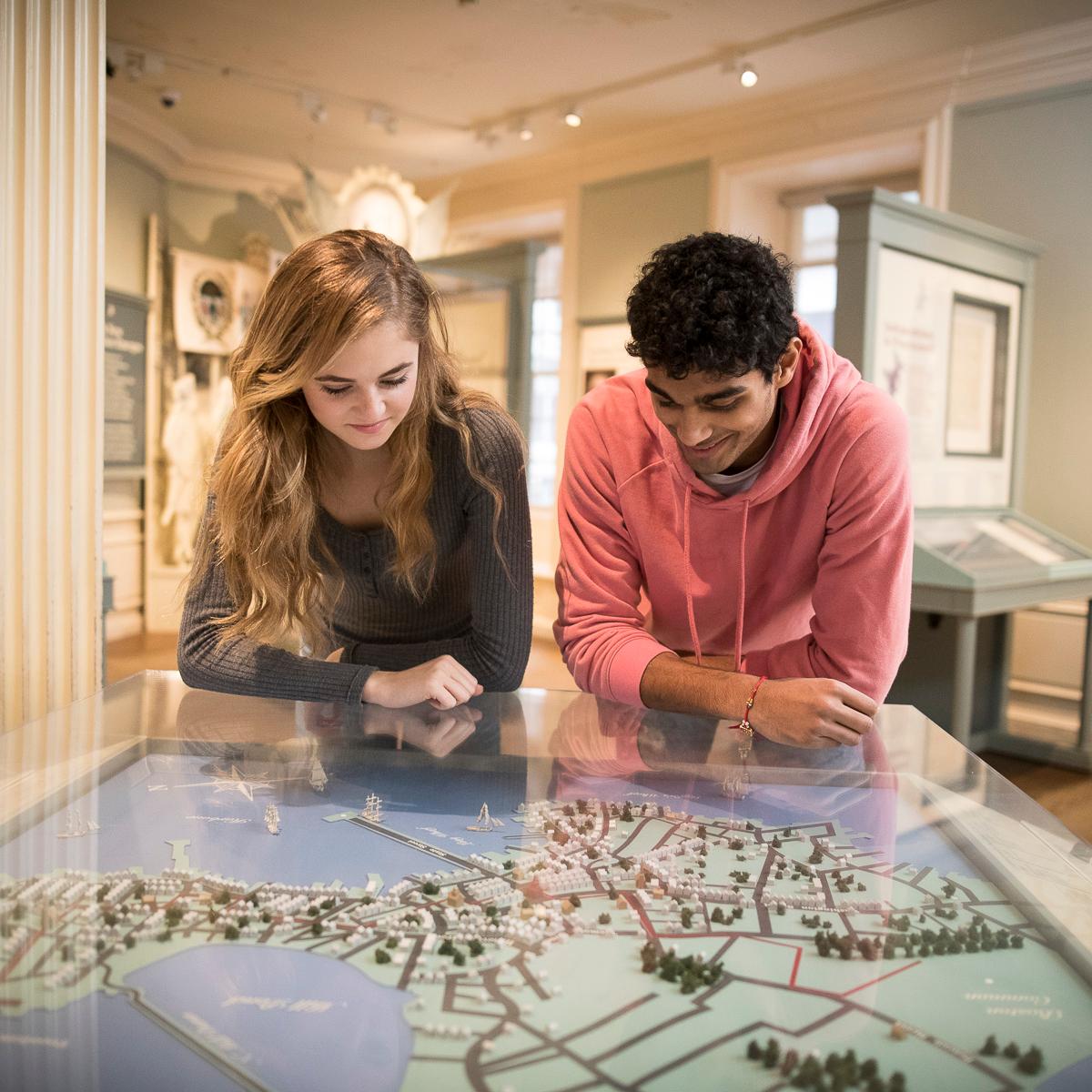 Two youth in an exhibit space, leaning over an interactive map table and looking down at it.