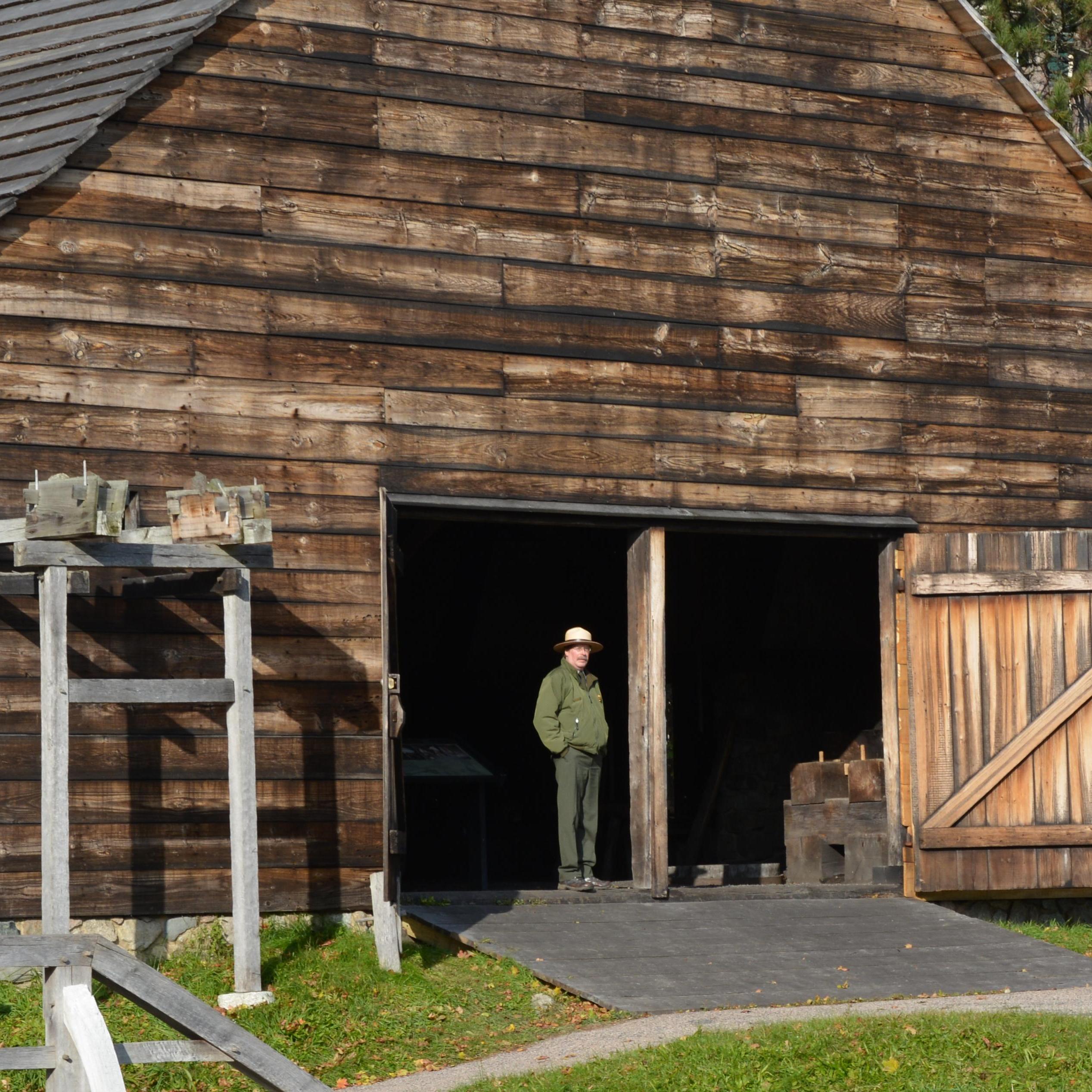 Ranger stands in doorway of a large wood-sided structure used to forge iron.