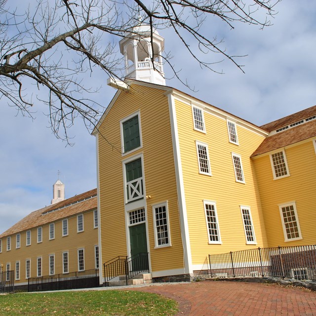 The Old Slater Mill, a yellow paneled building with a cupola. 