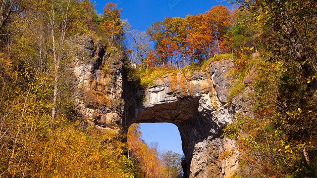 A large rock formation with an open area underneath and a rock bridge connecting two cliffs. 