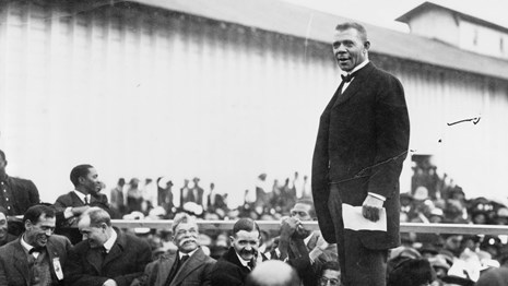 Booker T. Washington standing on a stage above a crowd.