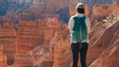 A woman stands before a landscape of redrock cliffs and spires