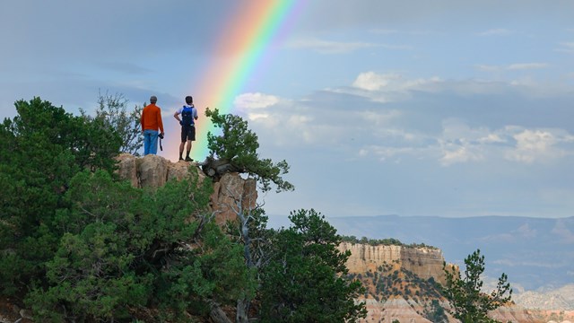Visitors stand at an elevated viewpoint with a rainbow above their heads.