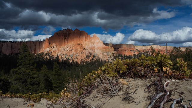 A large land formation with irregular red rock structures under dark storm clouds