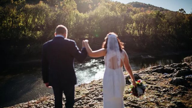 A bride and groom holding hands facing the river.