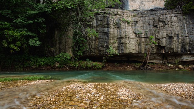 A shallow, clear river flows over a bed of small pebbles in the foreground. 