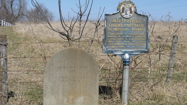 A stone marker next to an upright sign in a farm field.