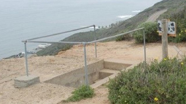 Metal hand railing wraps around 3 sides of concrete steps that go into the dirt.  