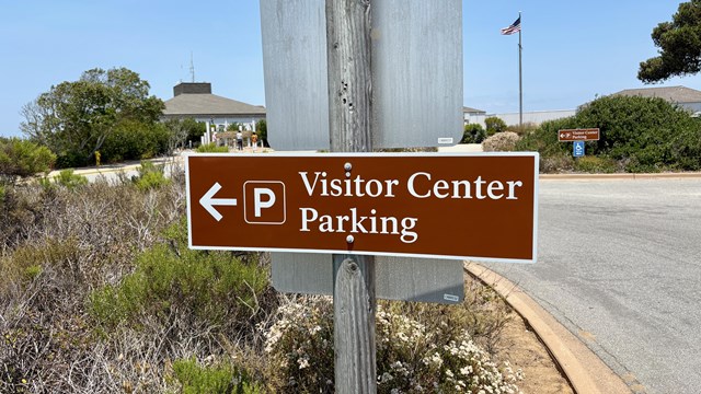 Brown sign with arrow: "Visitor Center Parking" and a parking symbol, points left.