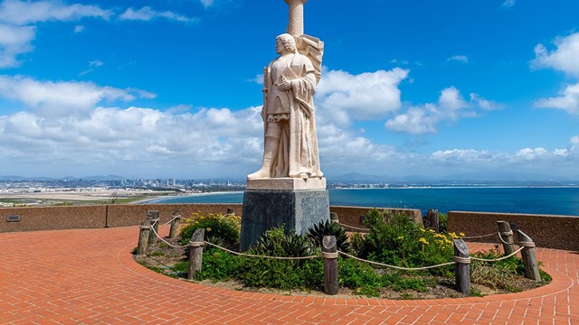 A statue of Juan Rodriguez Cabrillo with a scenic view of the bay in the background.