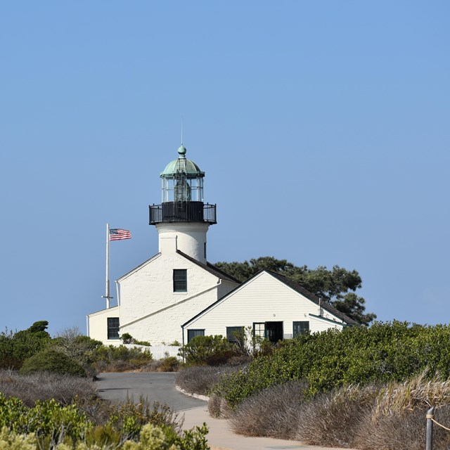 a white, unlit lighthouse and a flagpole with a raised American flag, all under a cloudless blue sky