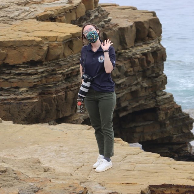 Previous CVA in Americorps dark blue uniform waving “hello” as she explores the Coastal Trail.