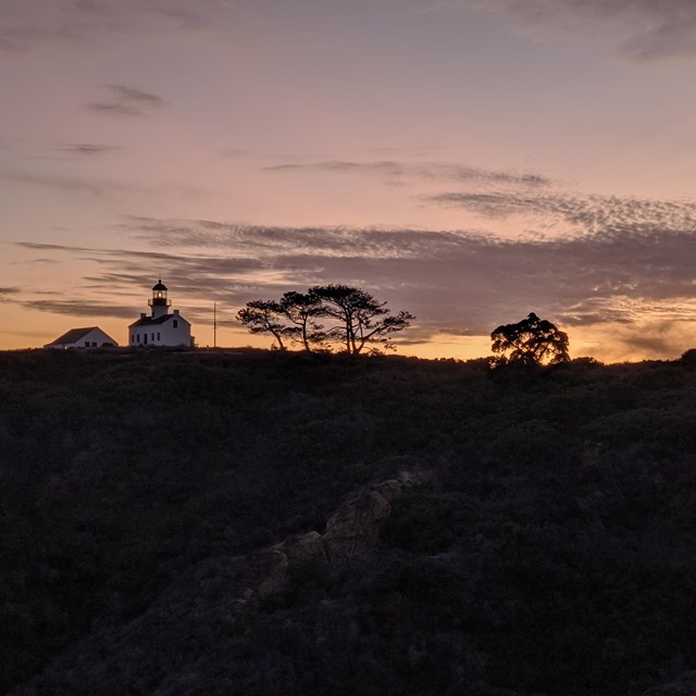 A pale orange glowing sunset behind the Old Point Loma Lighthouse.