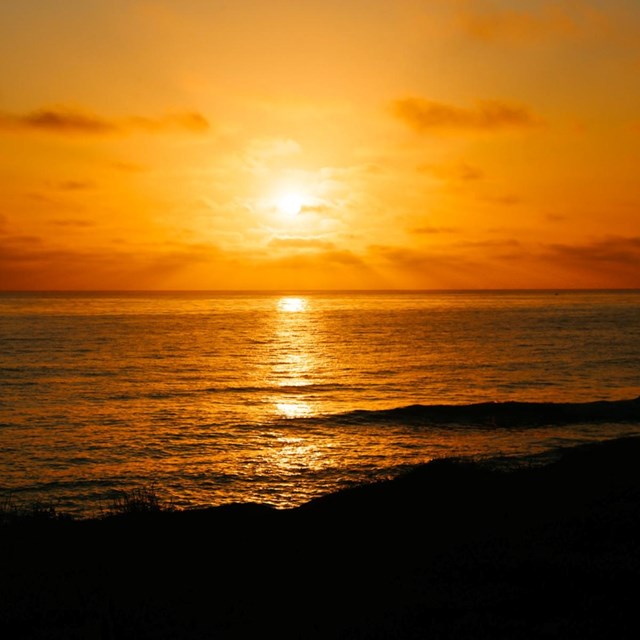 The bright orange sun is setting over the Pacific Ocean and the colors are reflecting on the water’s