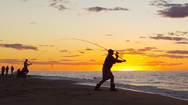 The silhouettes of fishermen are framed against a brilliant sunset.