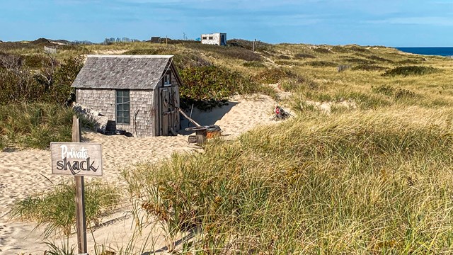 A small wooden shack nestled amongst sandy dunes.