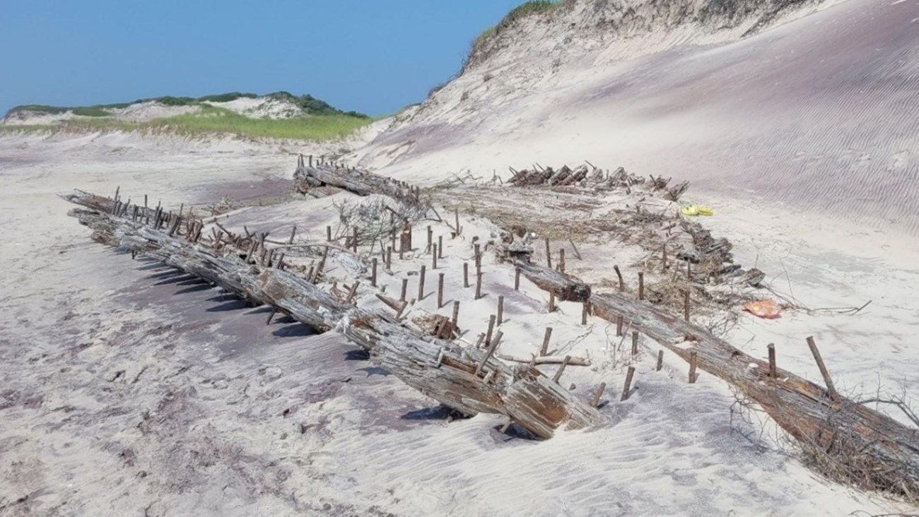 A shipwreck pokes out of the sand on the beach.
