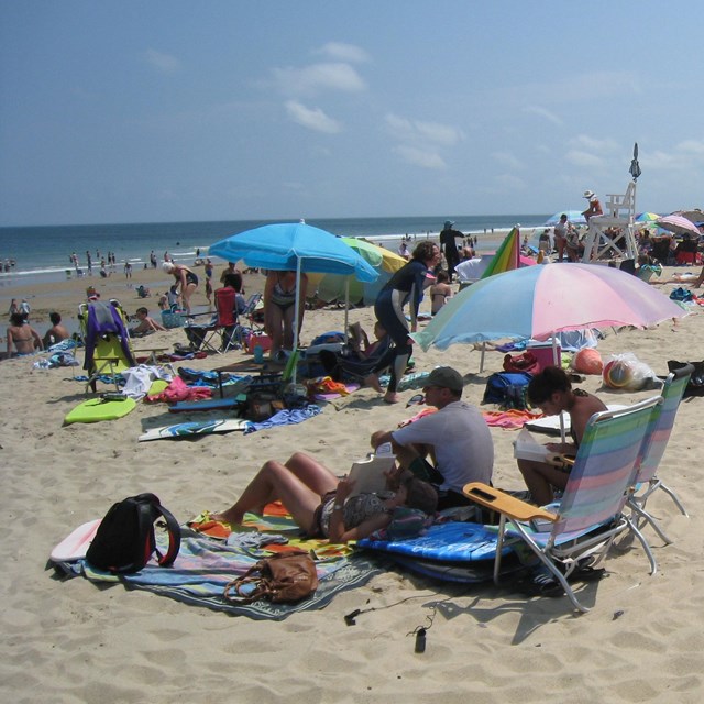 Beach goers enjoy the sun and surf with blankets and colorful umbrellas.