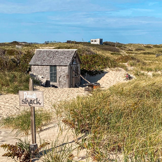 A small wooden shack nestled amongst sandy dunes.