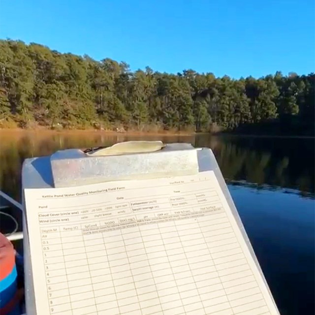 A data sheet is held up in front of a pond.