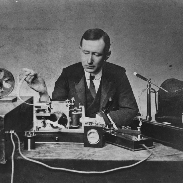 Black and white photograph showing a man in front a telegraph reciever.