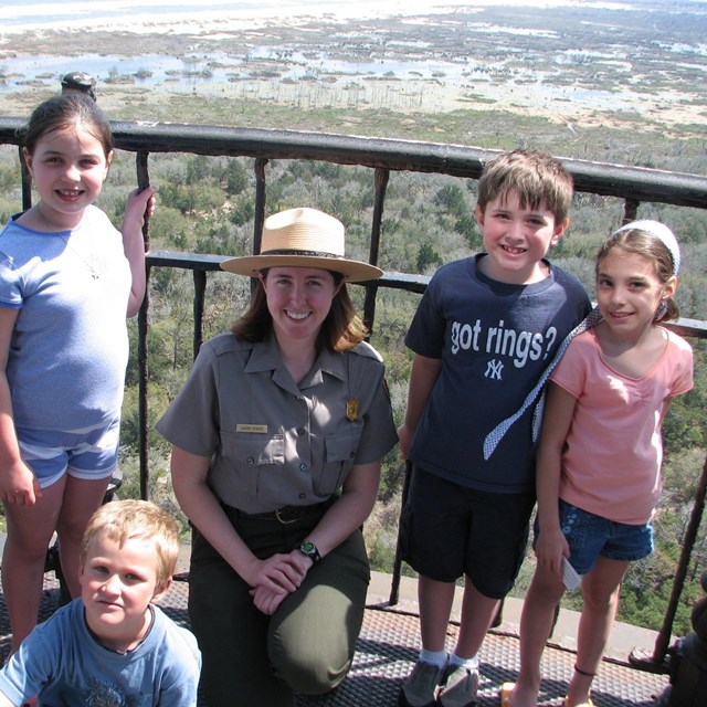 color photo of a ranger kneeling in the center of five kids who are standing