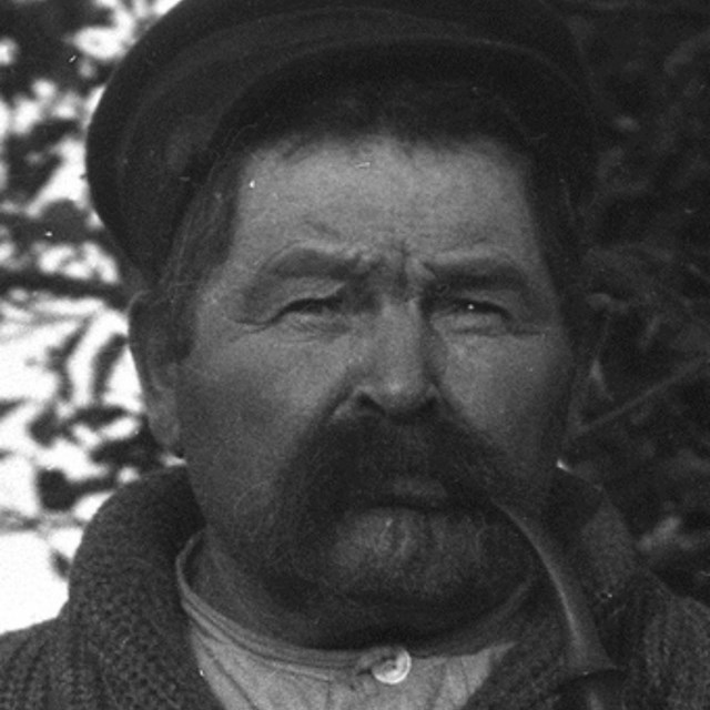 black and white close up photo of a mans face. He is wearing a hat and has a mustache.